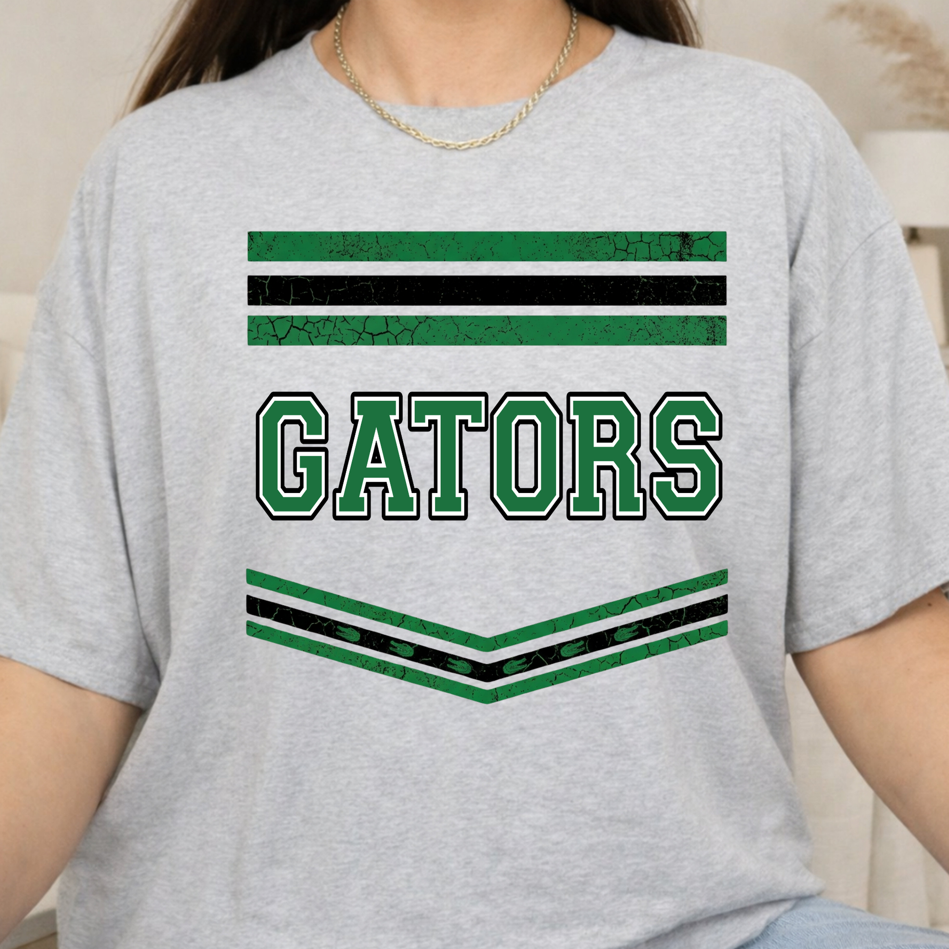 A person wearing a light heather gray t-shirt with a distressed green and black 'GATORS' collegiate graphic on the front.