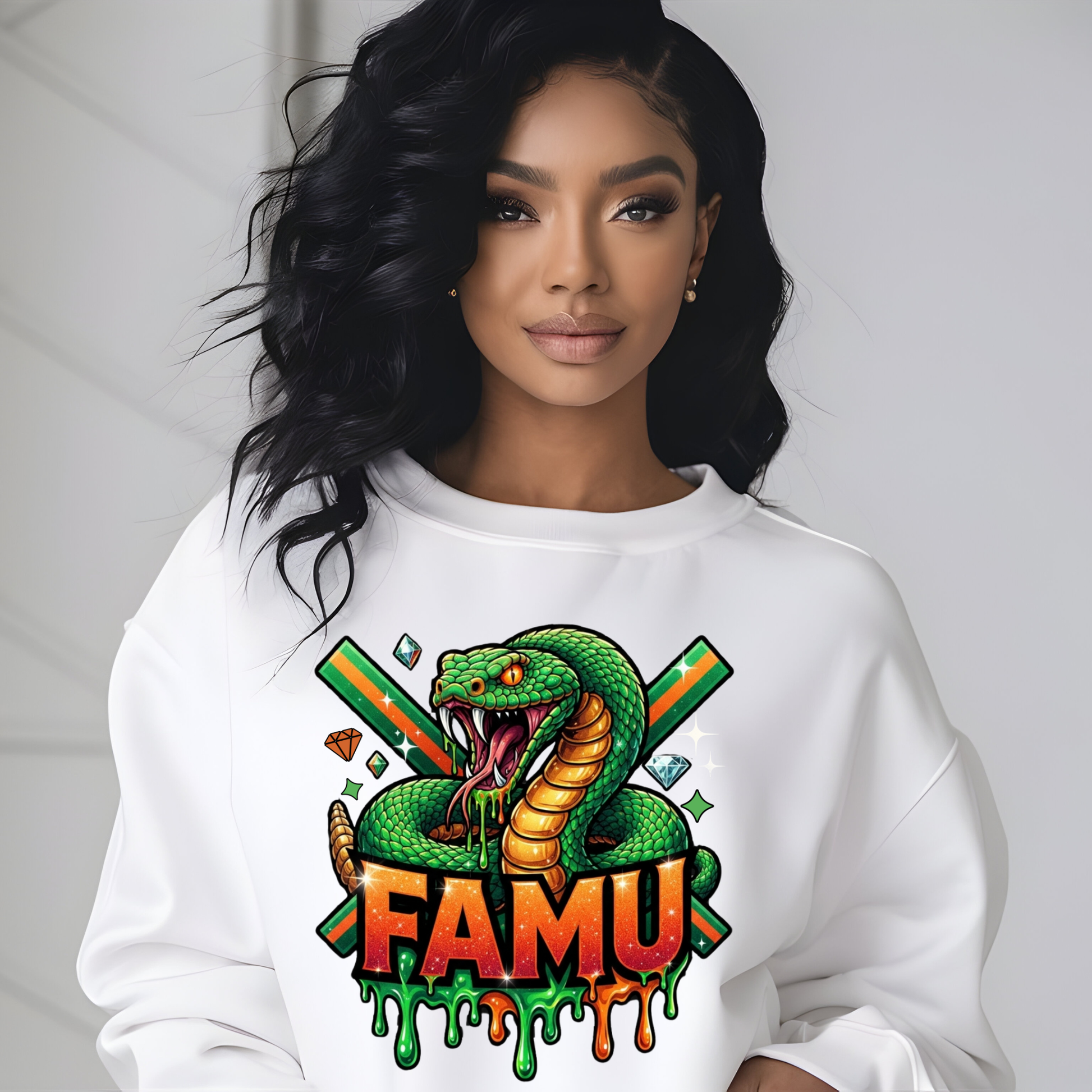 A woman wearing a white crewneck sweatshirt with a colorful graphic of a green snake, crossed green and orange sticks, and the word 'FAMU' in dripping orange and green letters.