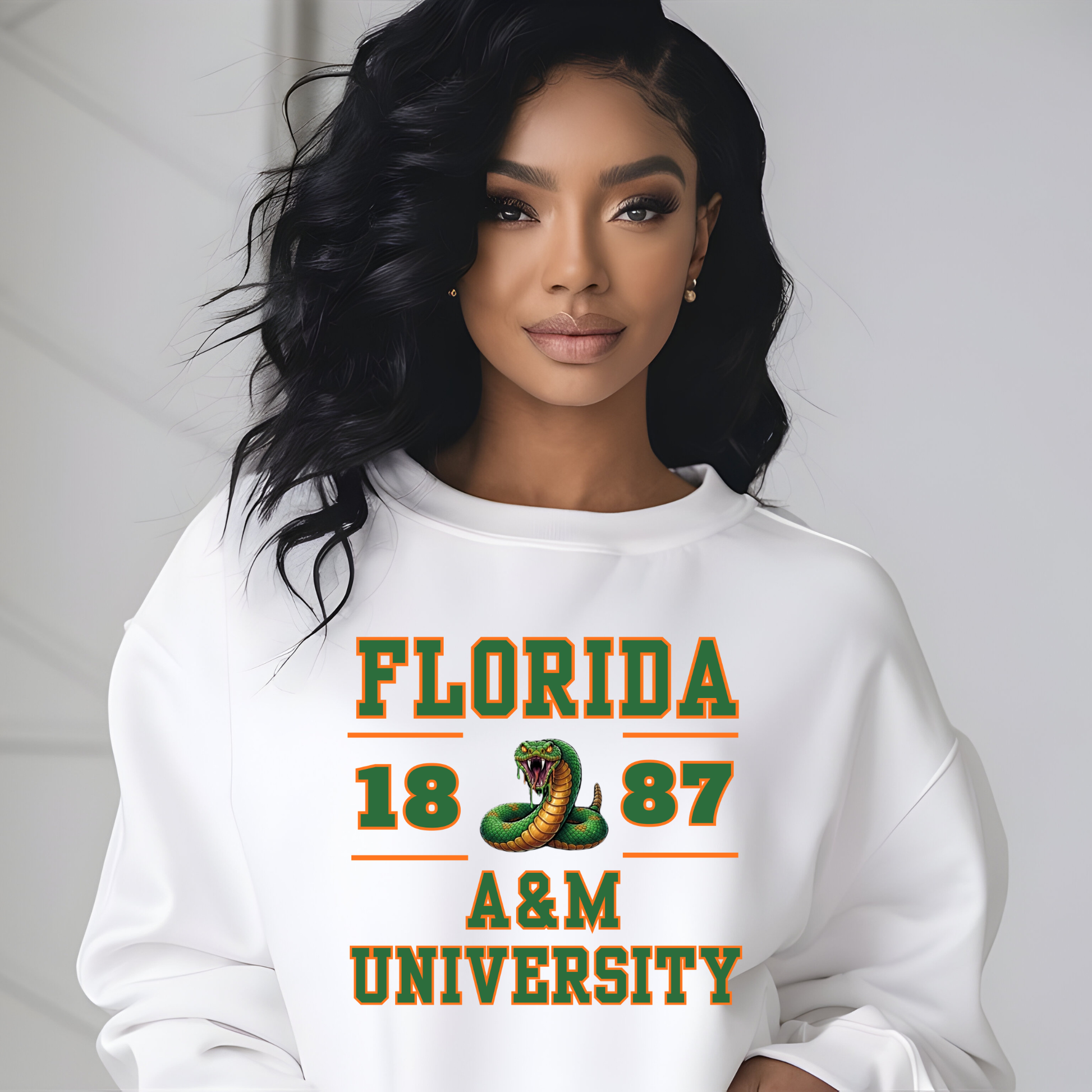 A woman wearing a white crewneck sweatshirt with a green and orange graphic that reads 'FLORIDA 1887 A&M UNIVERSITY' with a snake illustration, posed against a light gray background.