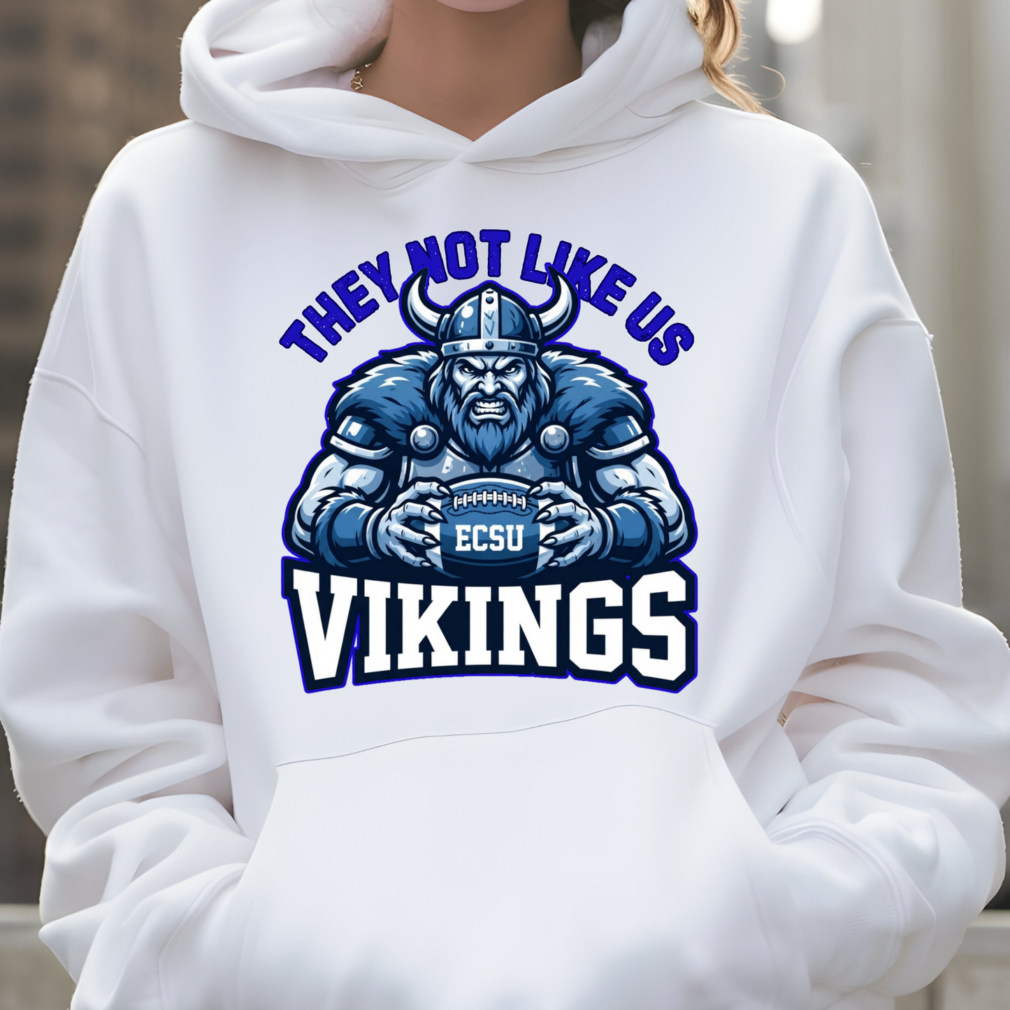 A person wearing a white pullover hoodie with a large blue and navy graphic on the chest featuring a Viking holding a football and the text 'THEY NOT LIKE US VIKINGS' with 'ECSU' on the helmet.
