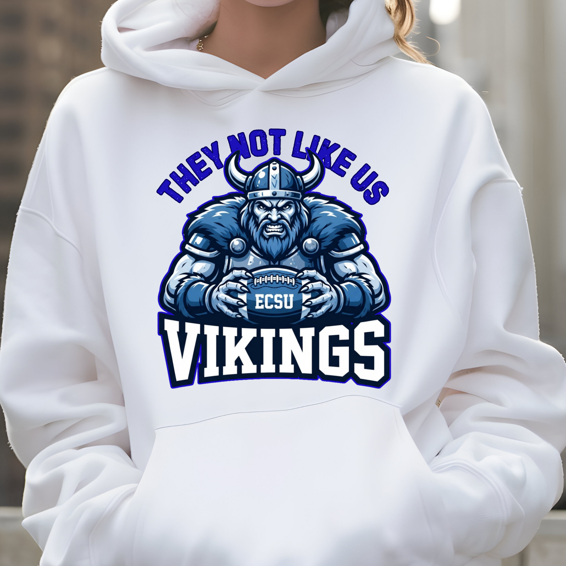 A person wearing a white pullover hoodie with a large blue and navy graphic on the chest featuring a Viking holding a football and the text 'THEY NOT LIKE US VIKINGS' with 'ECSU' on the helmet.