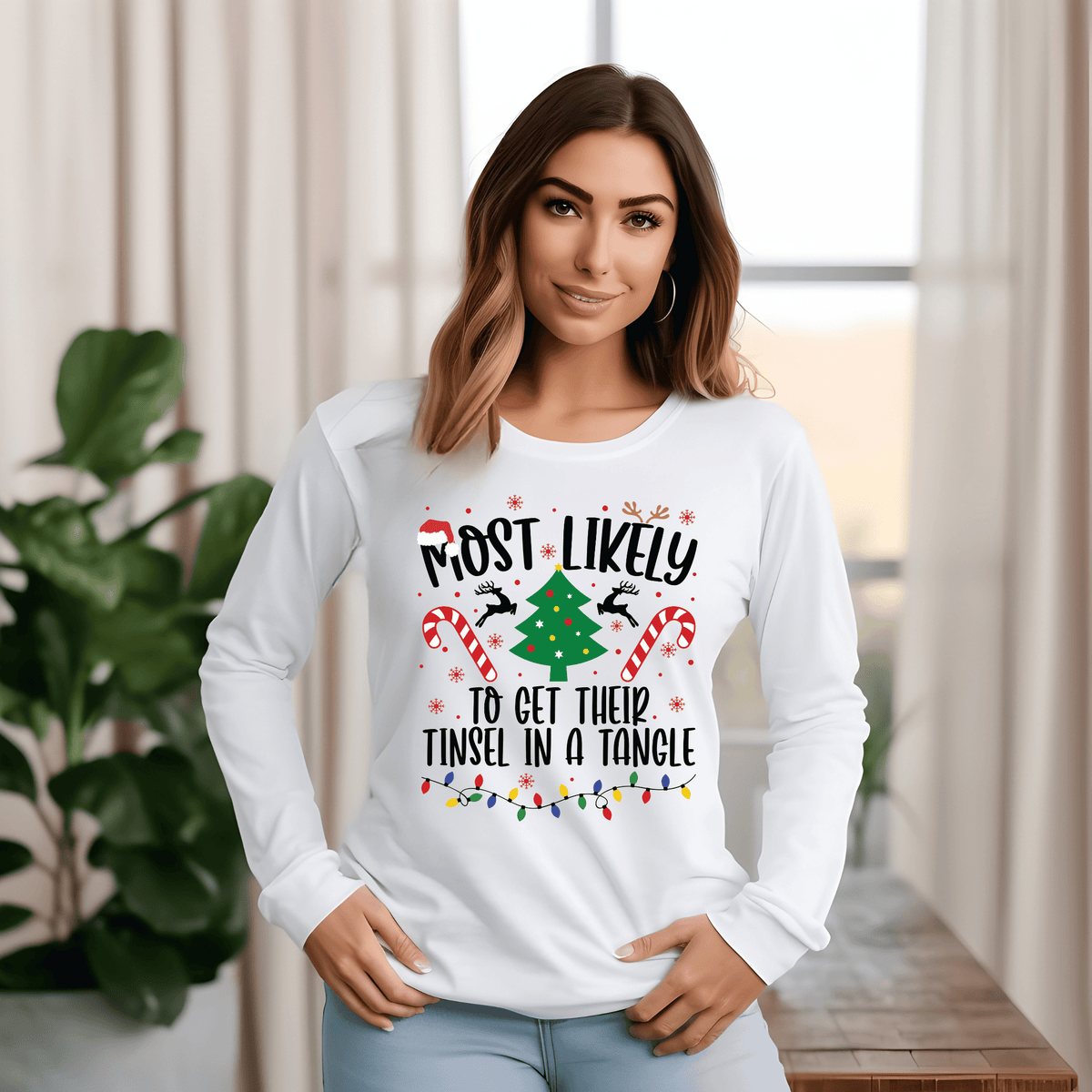 A woman modeling a white long-sleeve crewneck t-shirt with a festive Christmas graphic that reads 'MOST LIKELY TO GET THEIR TINSEL IN A TANGLE' with candy canes, a Christmas tree, and holiday lights.