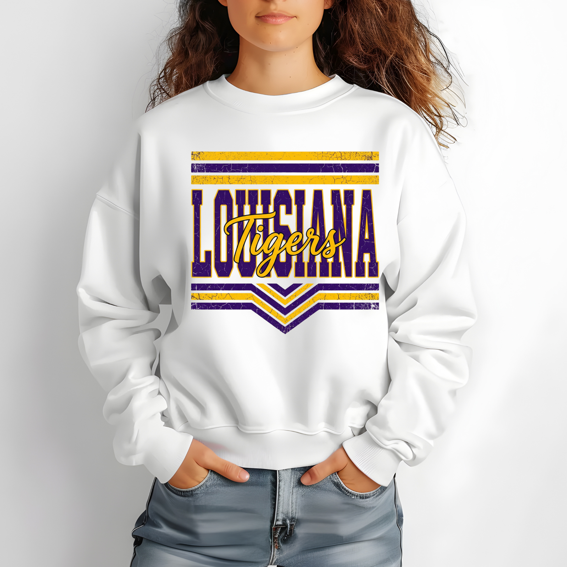 A person wearing a white crewneck sweatshirt with a distressed purple and yellow 'Louisiana Tigers' graphic on the front, paired with light blue jeans against a light gray background.