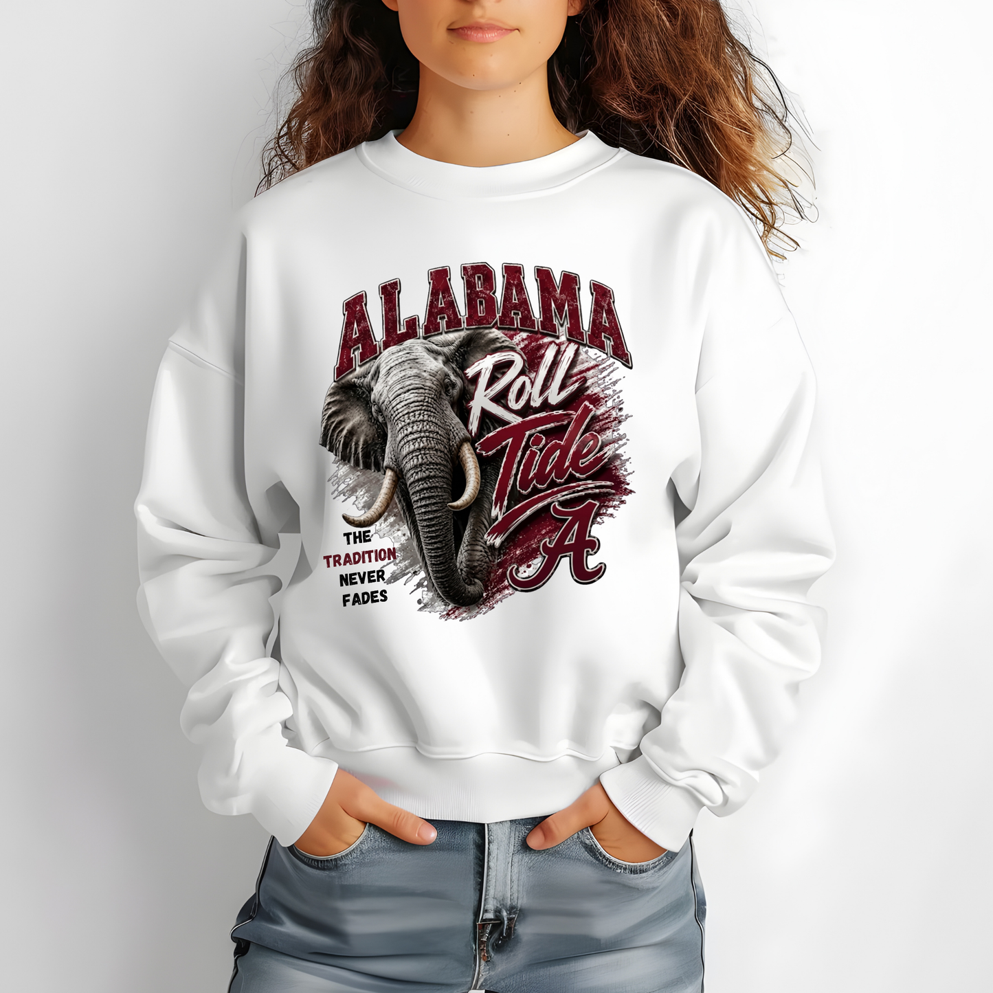 A woman wearing a white crewneck sweatshirt with a graphic print of an elephant and the text 'ALABAMA Roll Tide' in red and black, paired with blue jeans against a plain white background.