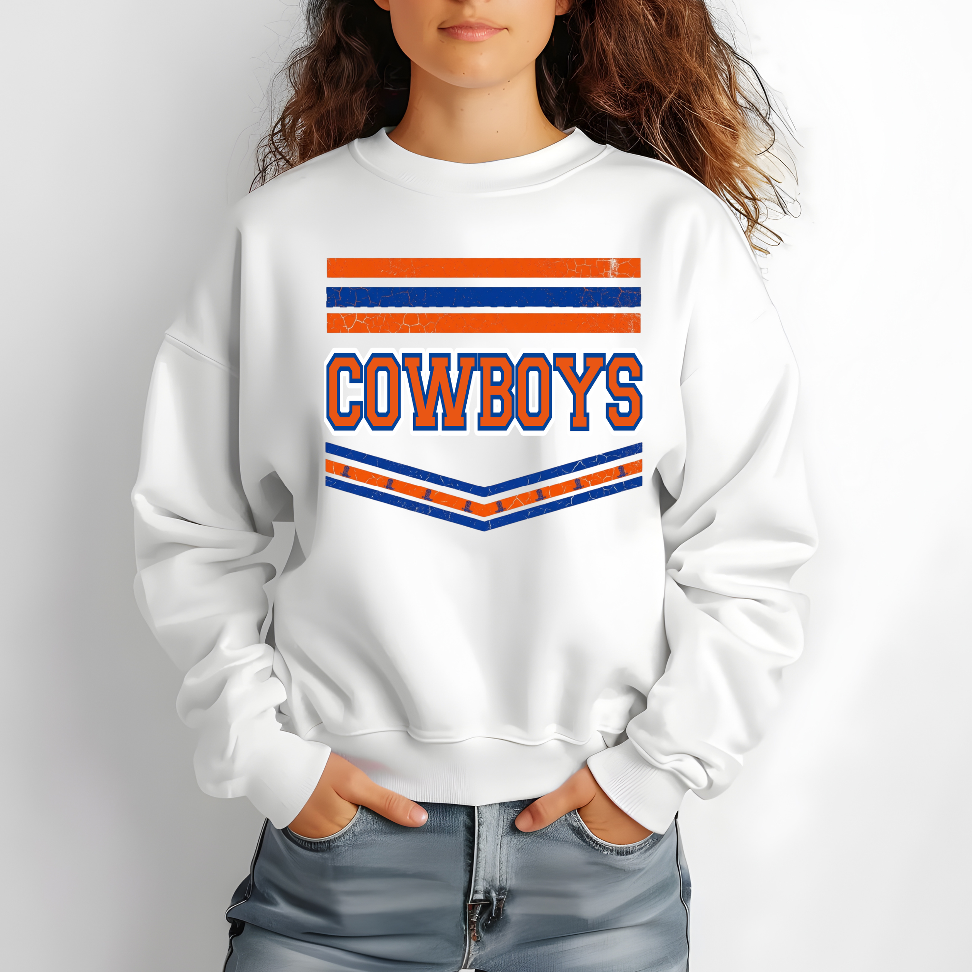 A person wearing a white crewneck sweatshirt with a distressed orange and blue 'COWBOYS' graphic on the chest, paired with light blue jeans against a light gray background.