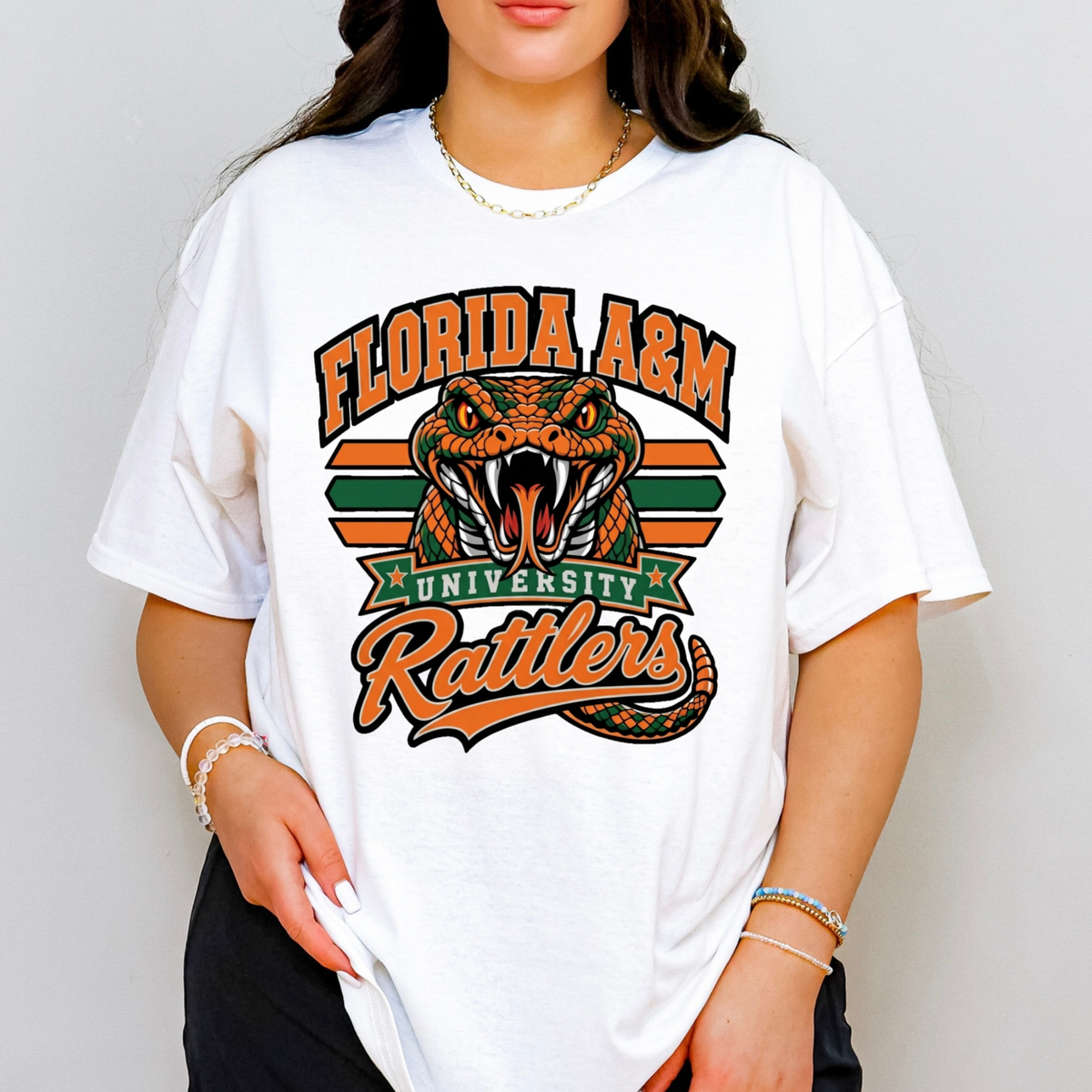 A woman wearing a white oversized graphic T-shirt featuring the Florida A&M University Rattlers design with an orange and green rattlesnake and the words 'FLORIDA A&M UNIVERSITY Rattlers' on the front.