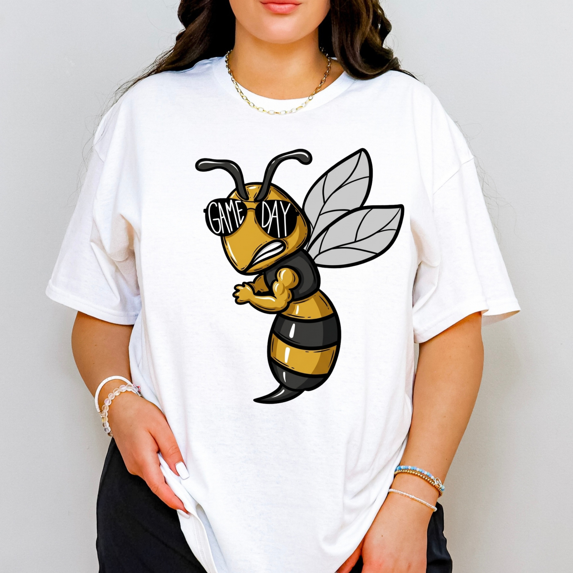 A woman wearing a white oversized graphic t-shirt featuring a cartoon bee wearing black and yellow stripes, sunglasses, and the words 'GAME DAY'.