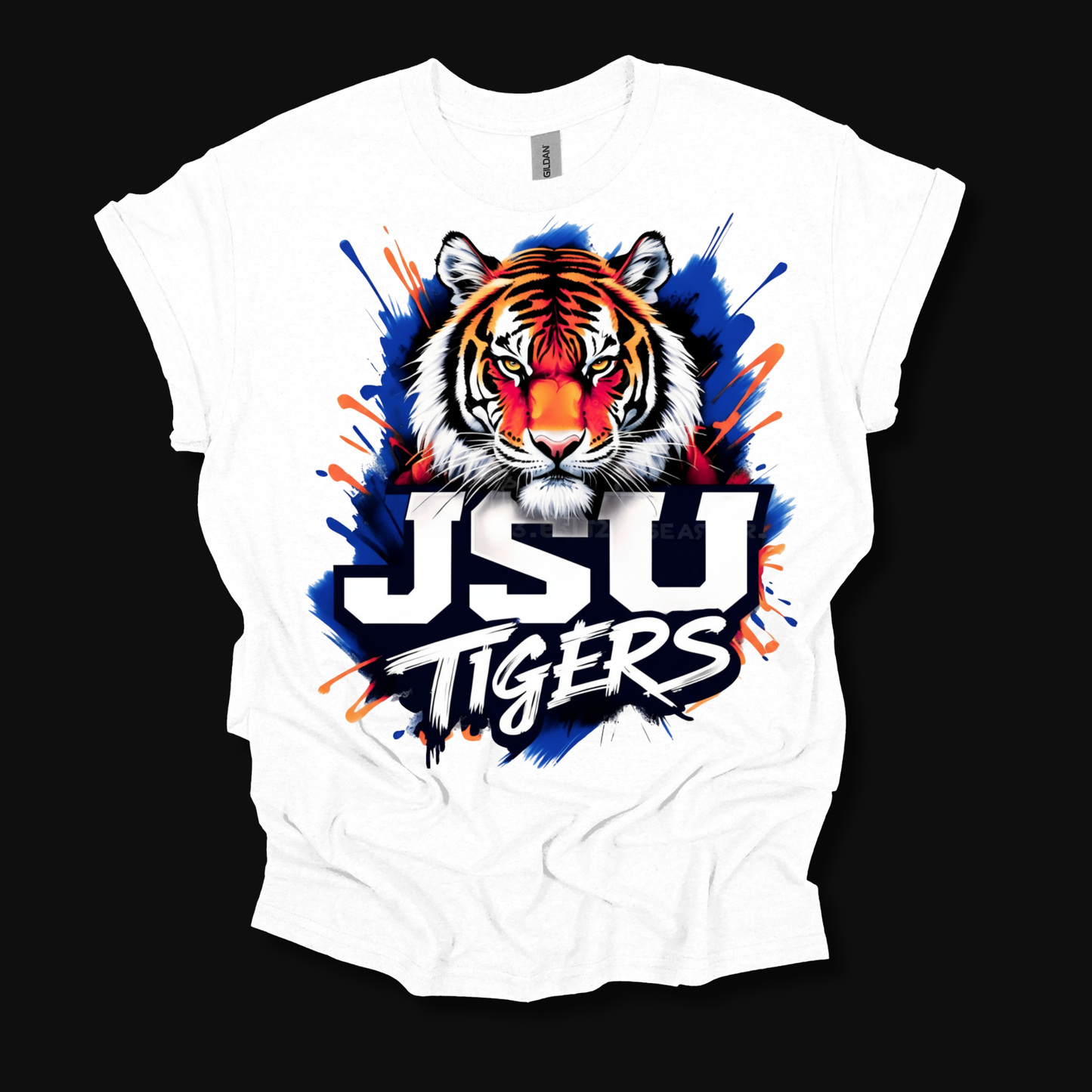 A white short-sleeve t-shirt with a vibrant graphic of a tiger's face and the text 'JSU TIGERS' in white with a black outline, set against a blue and orange paint splatter background, displayed on a solid black background.