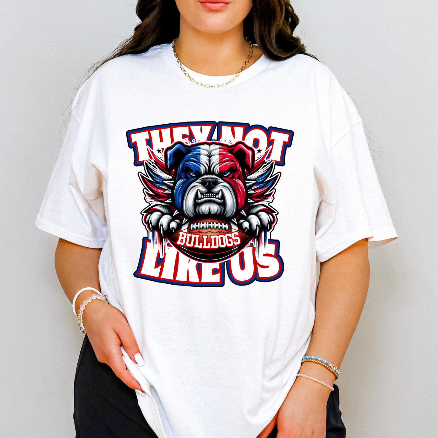 A woman wearing a white oversized graphic t-shirt with a bulldog mascot design and the text 'THEY NOT LIKE US' and 'BULLDOGS'.