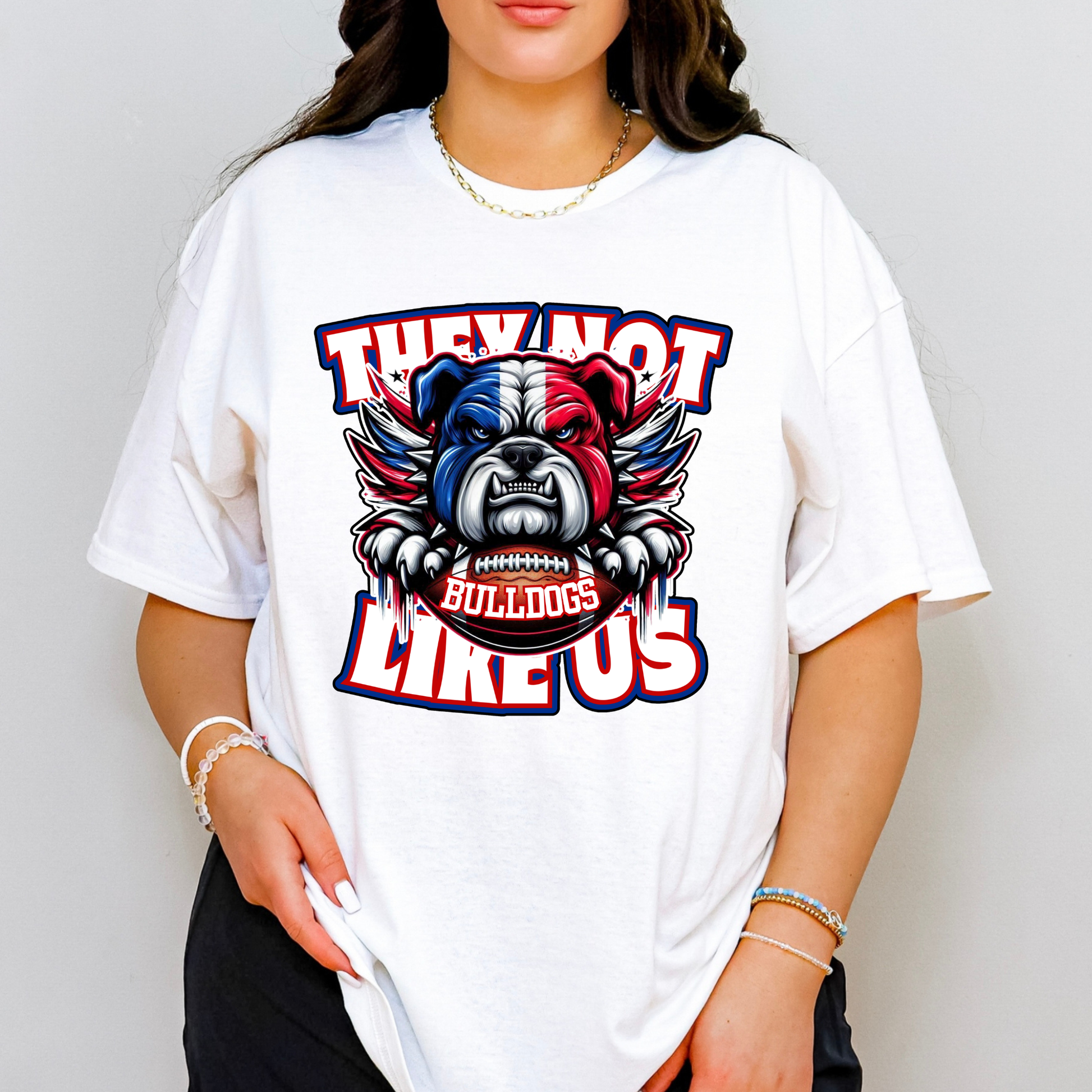 A woman wearing a white oversized graphic t-shirt with a bulldog mascot design and the text 'THEY NOT LIKE US' and 'BULLDOGS'.