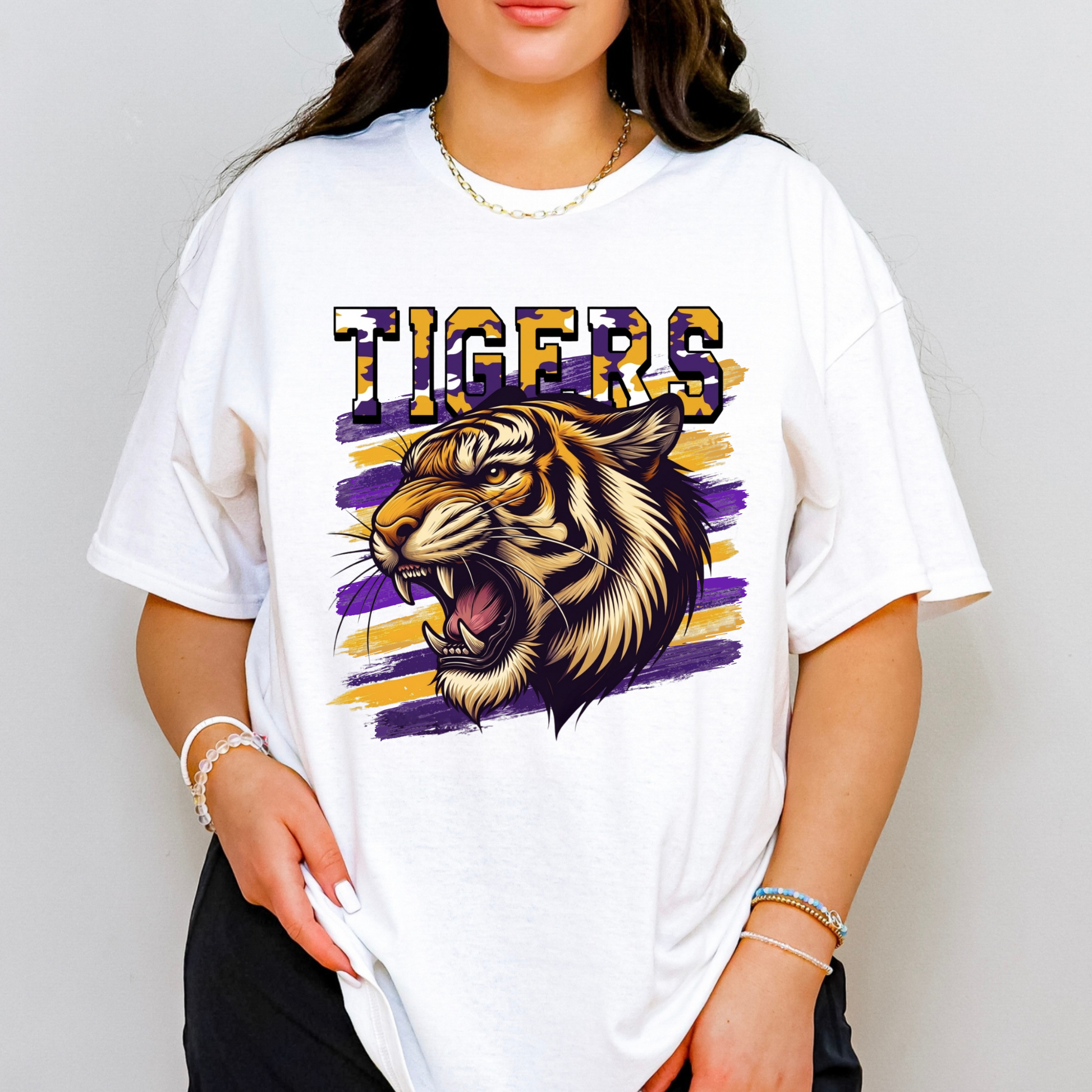A woman wearing a white oversized graphic t-shirt featuring a roaring tiger illustration and the word 'TIGERS' in purple, gold, and black.