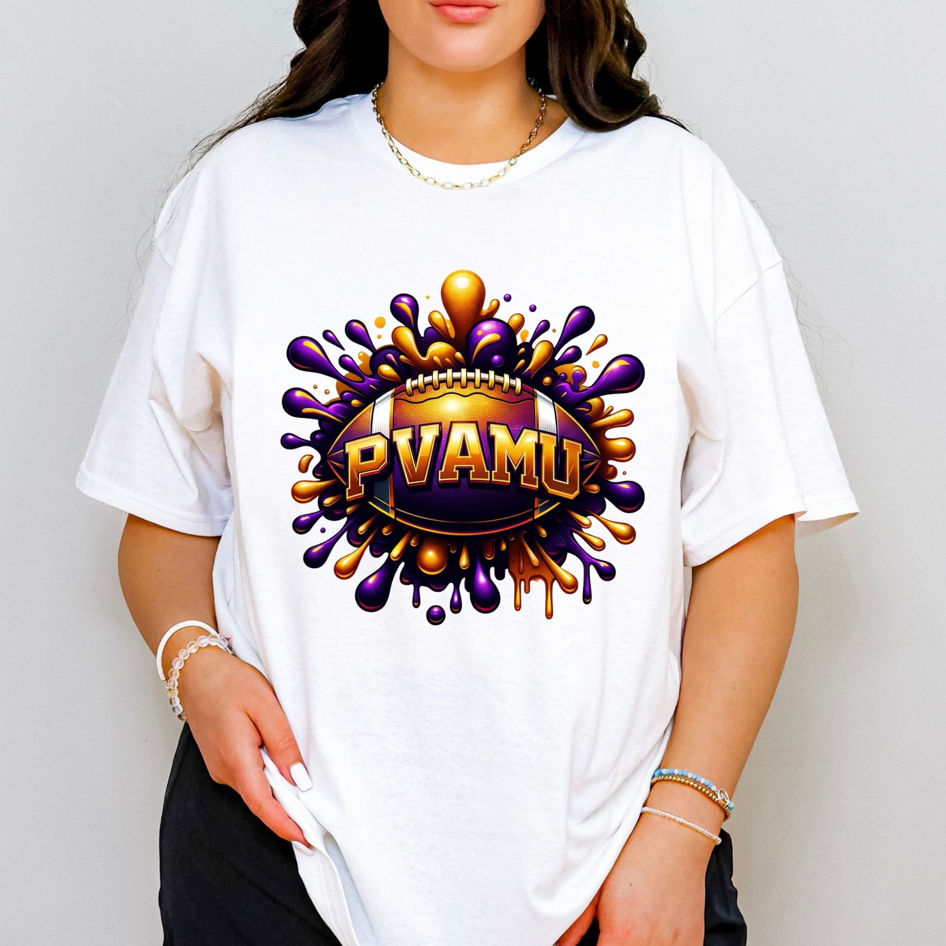 A woman wearing a white oversized t-shirt with a colorful graphic on the chest. The graphic features a football surrounded by purple and gold paint splatters with the text 'PVAMU' in gold.