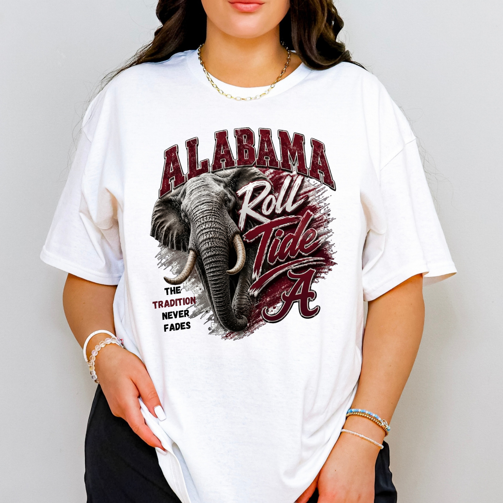 A woman wearing an oversized white graphic t-shirt featuring the Alabama Crimson Tide logo and an elephant design on the front, set against a plain light gray background.