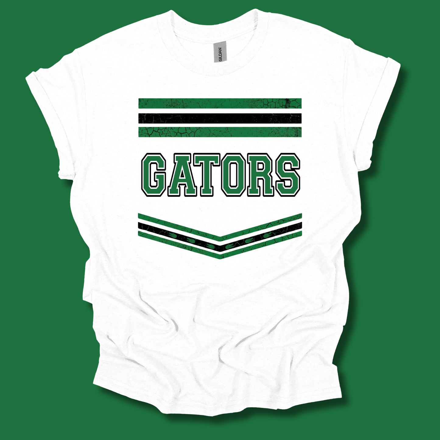 A white short-sleeve t-shirt with a green and black collegiate-style graphic featuring the word 'GATORS' and striped accents, displayed against a solid green background.