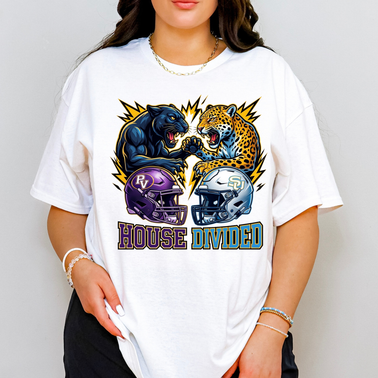 A woman wearing an oversized white graphic t-shirt featuring a stylized fight between a black panther and a leopard, with football helmets in purple and silver below and the text 'HOUSE DIVIDED'.