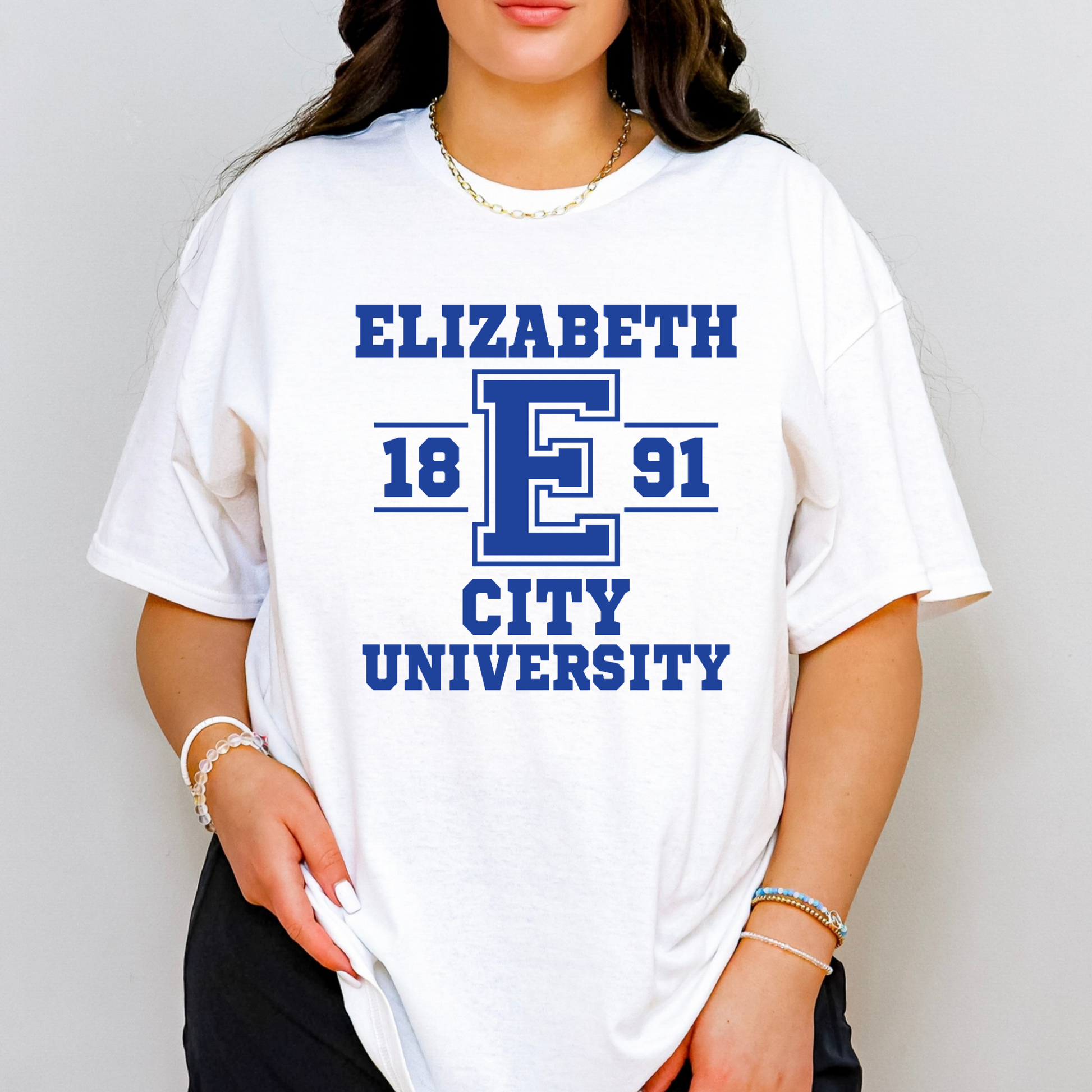 A woman wearing an oversized white t-shirt with a blue collegiate-style graphic that reads 'ELIZABETH 18 E 91 CITY UNIVERSITY'.