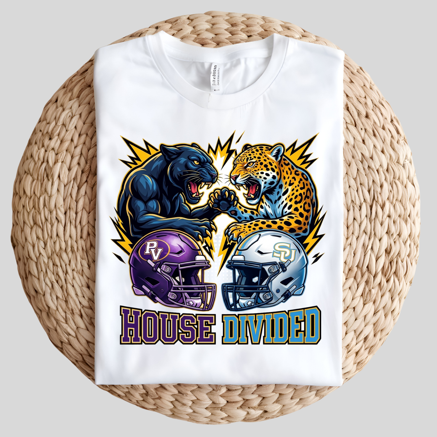 A white short-sleeve t-shirt with a colorful graphic of a black panther and a leopard facing off, with football helmets and the text 'HOUSE DIVIDED' underneath, displayed on a round woven straw mat against a light gray background.