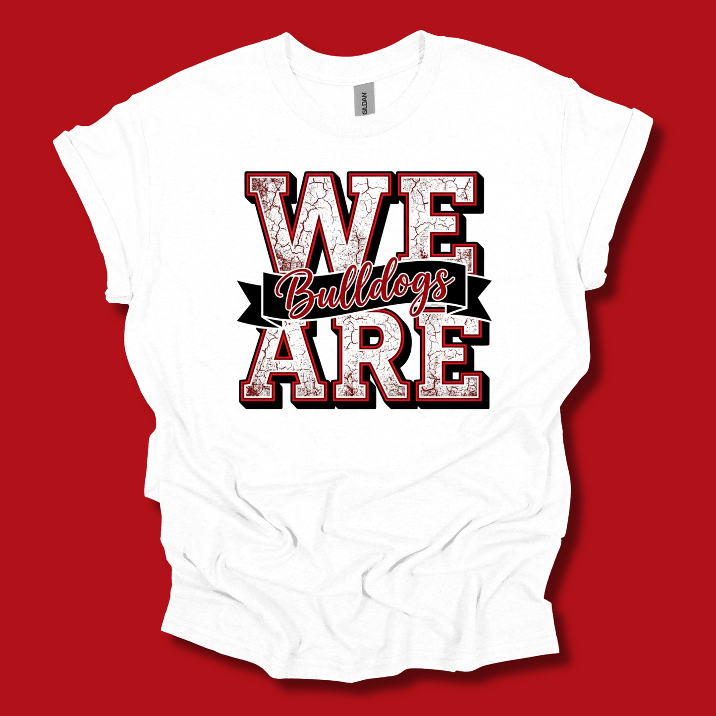 A white short-sleeve t-shirt with a distressed graphic reading 'WE ARE' in red and black, with 'Bulldogs' in red script across the center, laid flat against a solid red background.