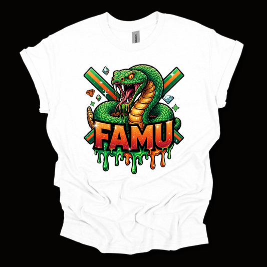 A white short-sleeve t-shirt with a colorful graphic print of a green snake, crossed green and orange swords, dice, and the word 'FAMU' in dripping orange and green letters, shown against a solid black background.