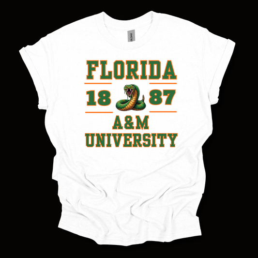 A white short-sleeve t-shirt with a green and orange graphic print reading 'FLORIDA 1887 A&M UNIVERSITY' and featuring a snake illustration, shown against a solid black background.