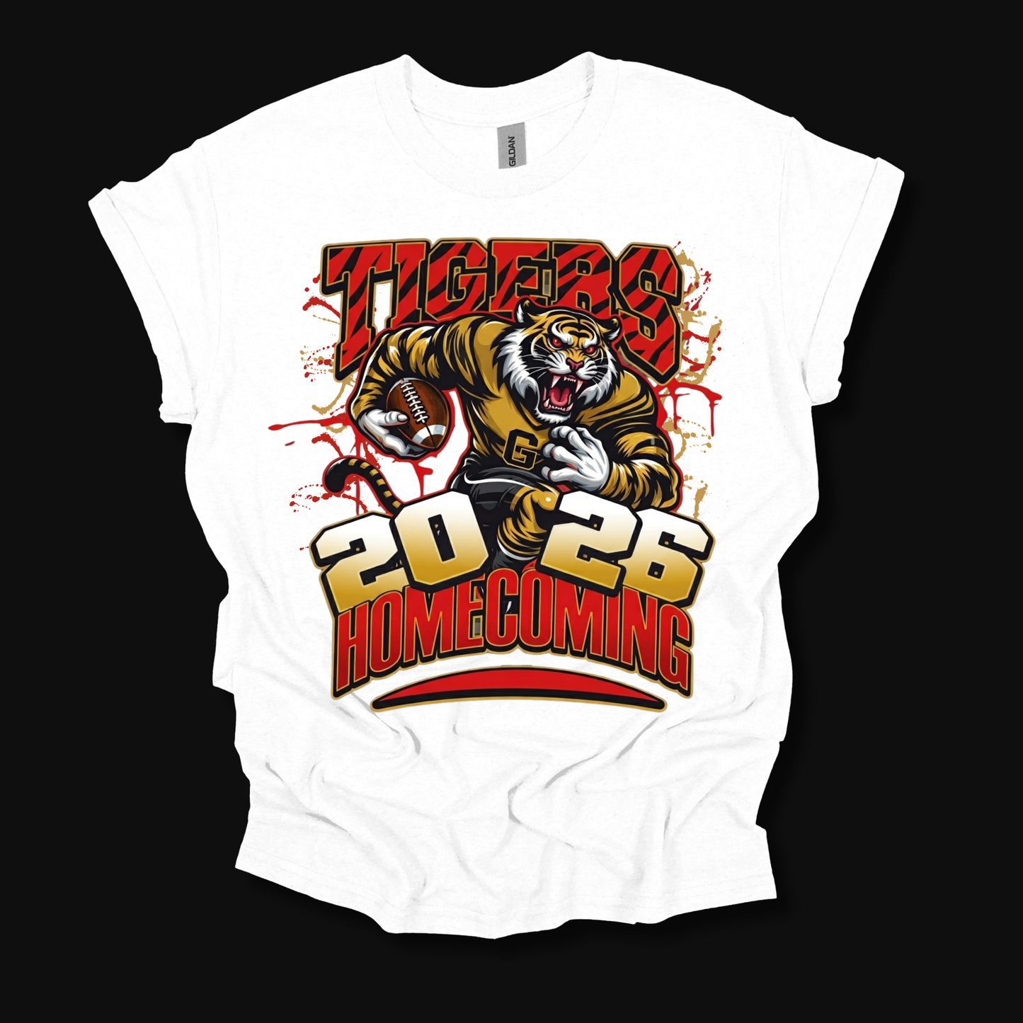 A white short-sleeve graphic t-shirt laid flat against a solid black background. The shirt features a large front print of a cartoon tiger holding a football, with the text 'TIGERS 2026 HOMECOMING' in red, yellow, and black.