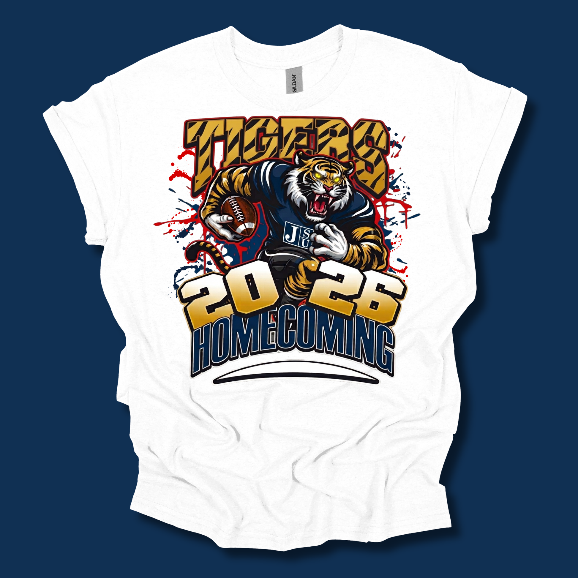 A white short-sleeve t-shirt with a large graphic print of a tiger mascot wearing a navy and gold uniform, with the text 'TIGERS', '2026', and 'HOMECOMING'. The shirt is displayed flat against a dark navy blue background.