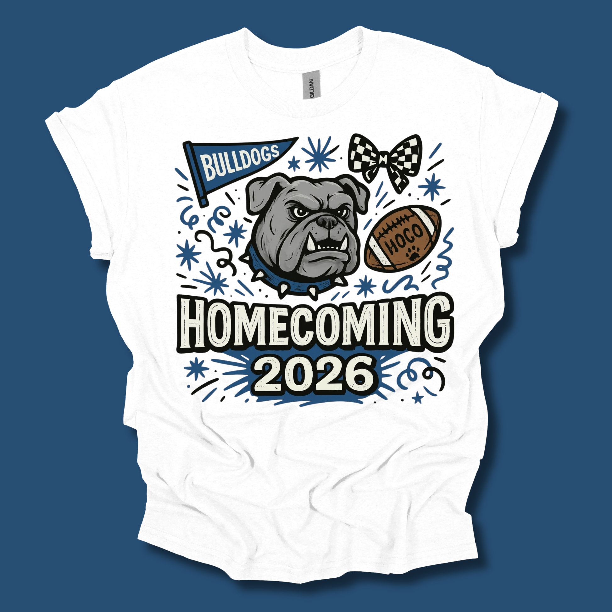 A white short-sleeve t-shirt with a graphic design on the front, featuring a bulldog, a football, a bow tie, and the text 'BULLDOGS HOMECOMING 2026' in blue, black, and brown, set against a solid dark blue background.