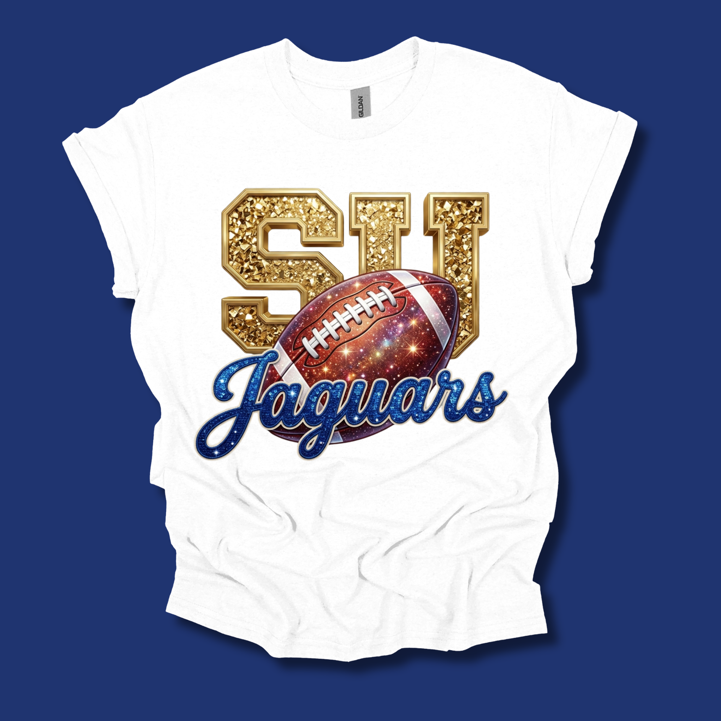 A white short-sleeve t-shirt with a graphic design featuring glittery gold 'SJ' letters, a football with a galaxy pattern, and 'Jaguars' in blue script, displayed against a solid dark blue background.