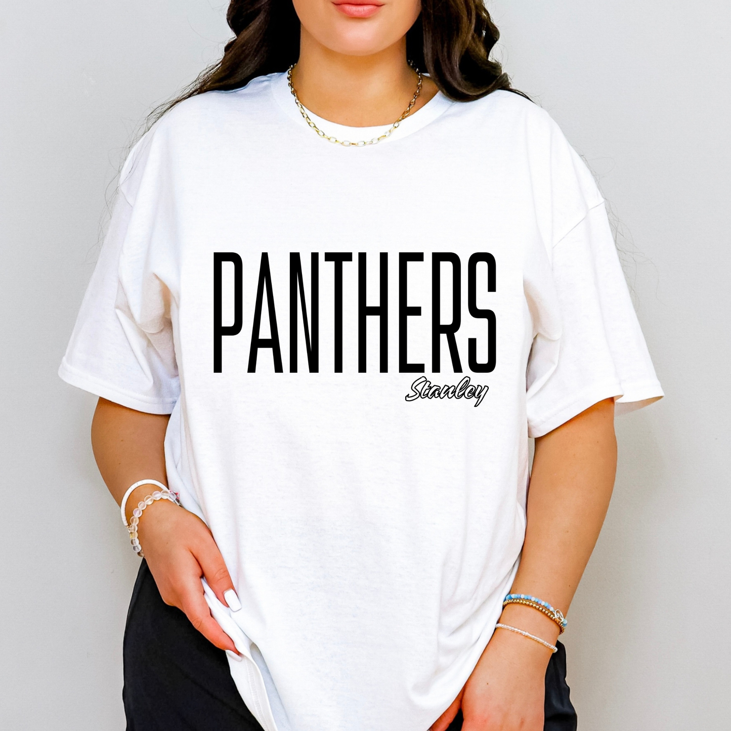 A woman wearing an oversized white t-shirt with 'PANTHERS' printed in bold black letters and 'Stanley' in script underneath, set against a plain light gray background.