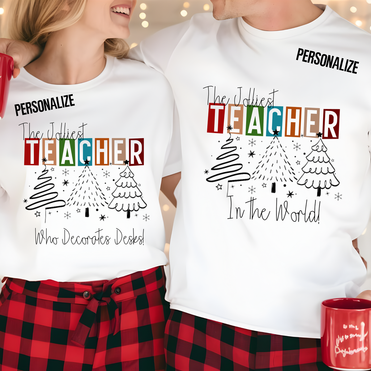 Two people wearing matching white custom holiday pajama shirts with a colorful 'Teacher' graphic, Christmas trees, and the text 'The Joliest Teacher In the World! Who Decorates Desks!'. The shirts have 'PERSONALIZE' printed at the top.