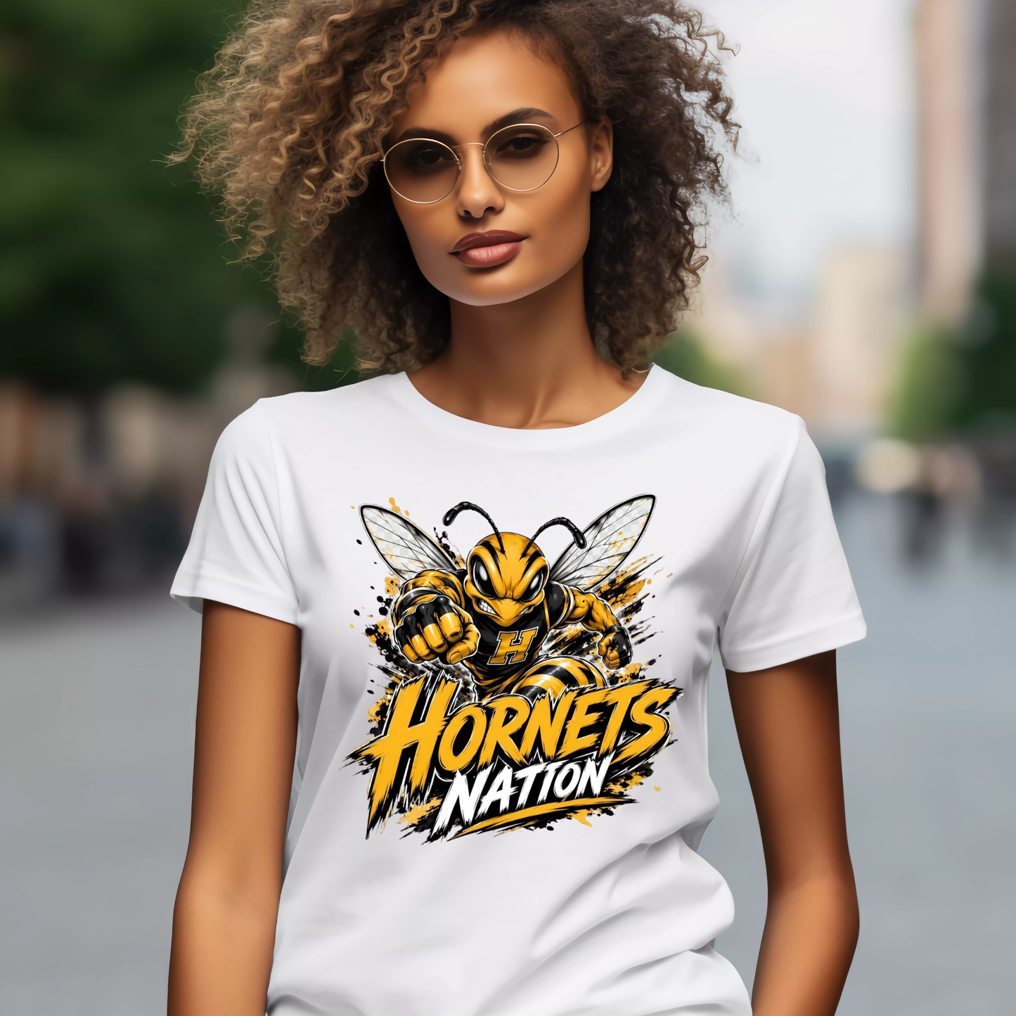 A woman wearing a white graphic t-shirt with a yellow and black hornet design and the text 'Hornets Nation' on the front, set against a blurred outdoor city background.