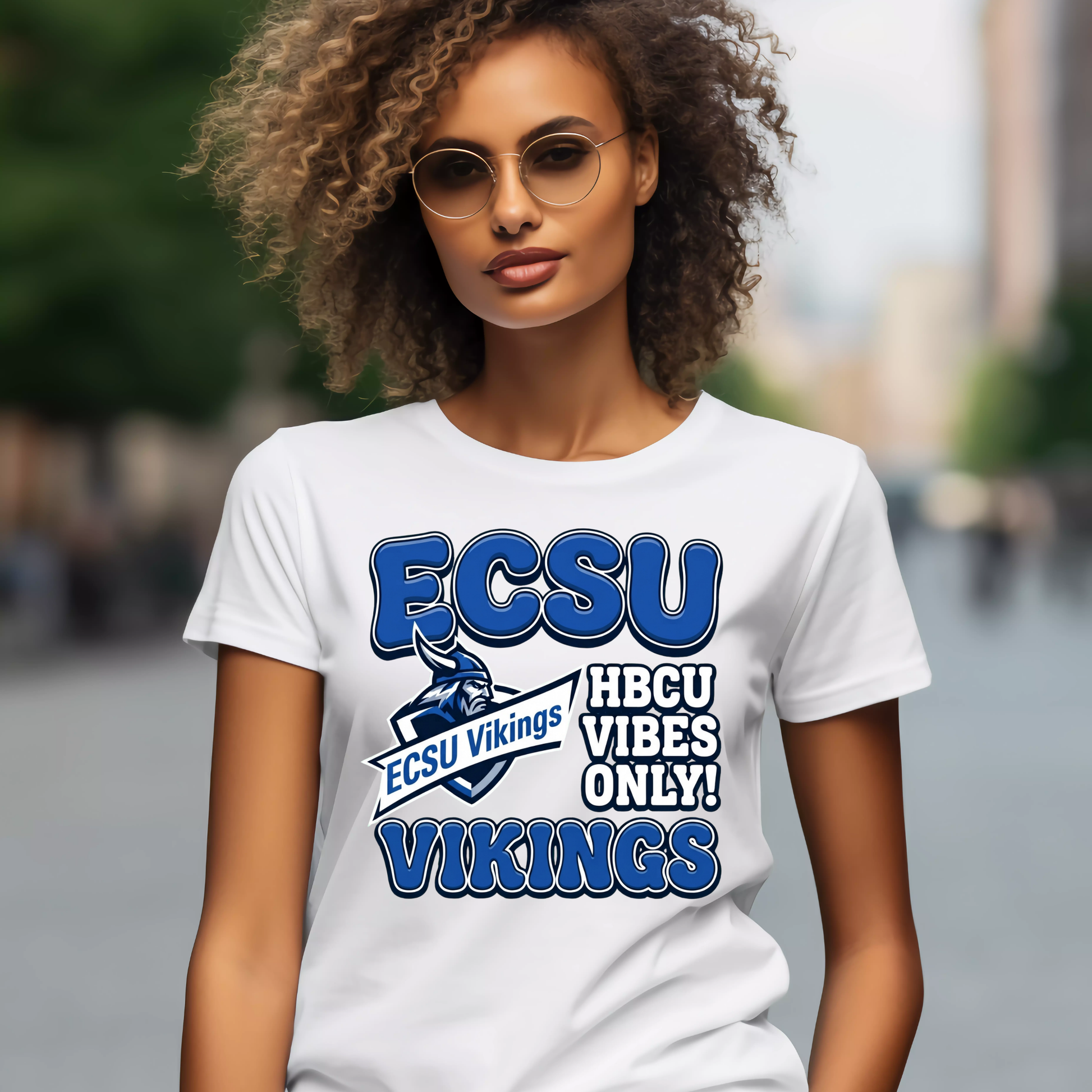 A woman wearing round glasses and a white graphic T-shirt with purple and gold text reading 'PRAIRE VIEW A&M PANTHERS I LOVE MY HBCU' and a panther mascot, photographed against a blurred outdoor street background.