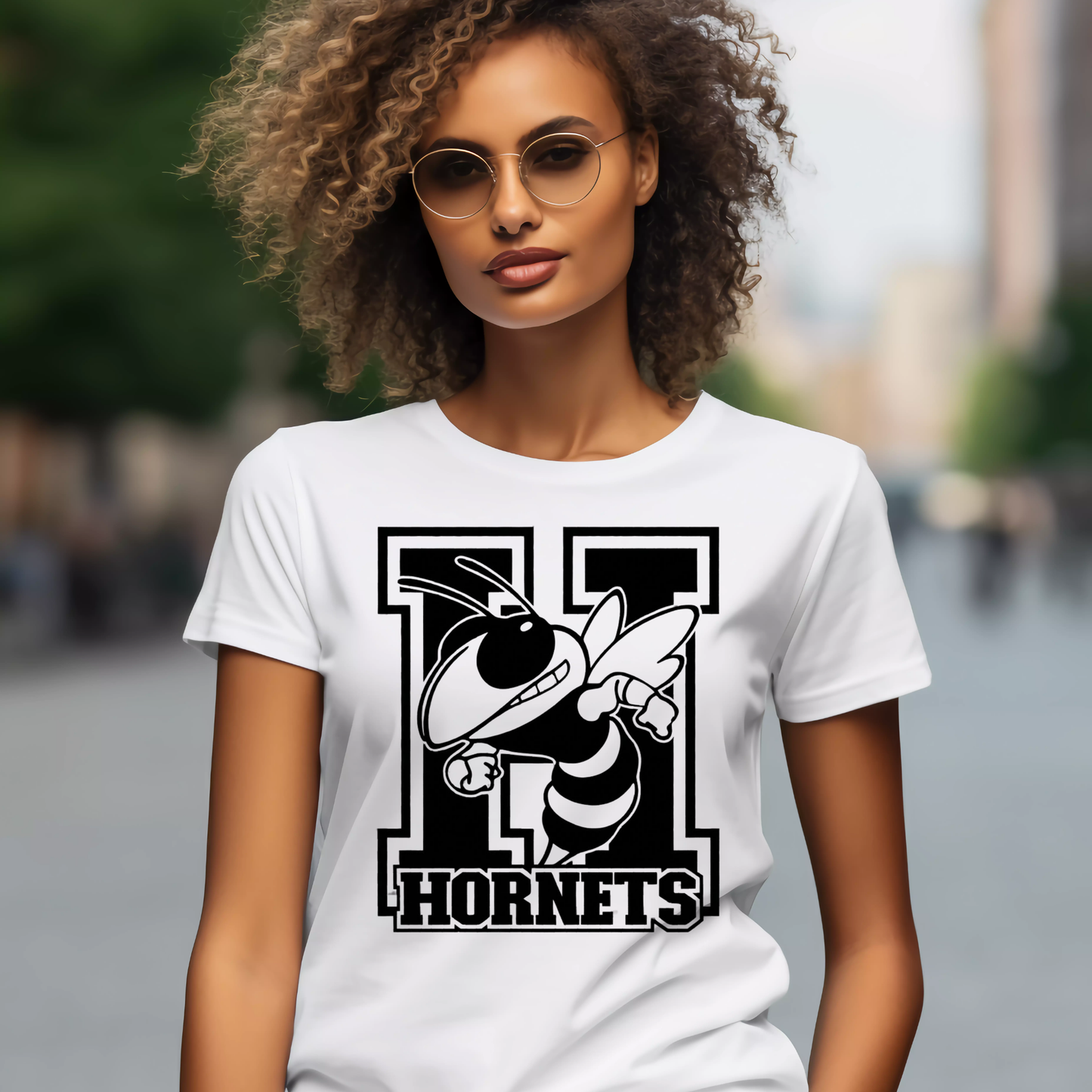 A woman wearing a white short-sleeve T-shirt with a large black and white hornet graphic and the word "HORNETS" on the front, photographed outdoors with a blurred city background.