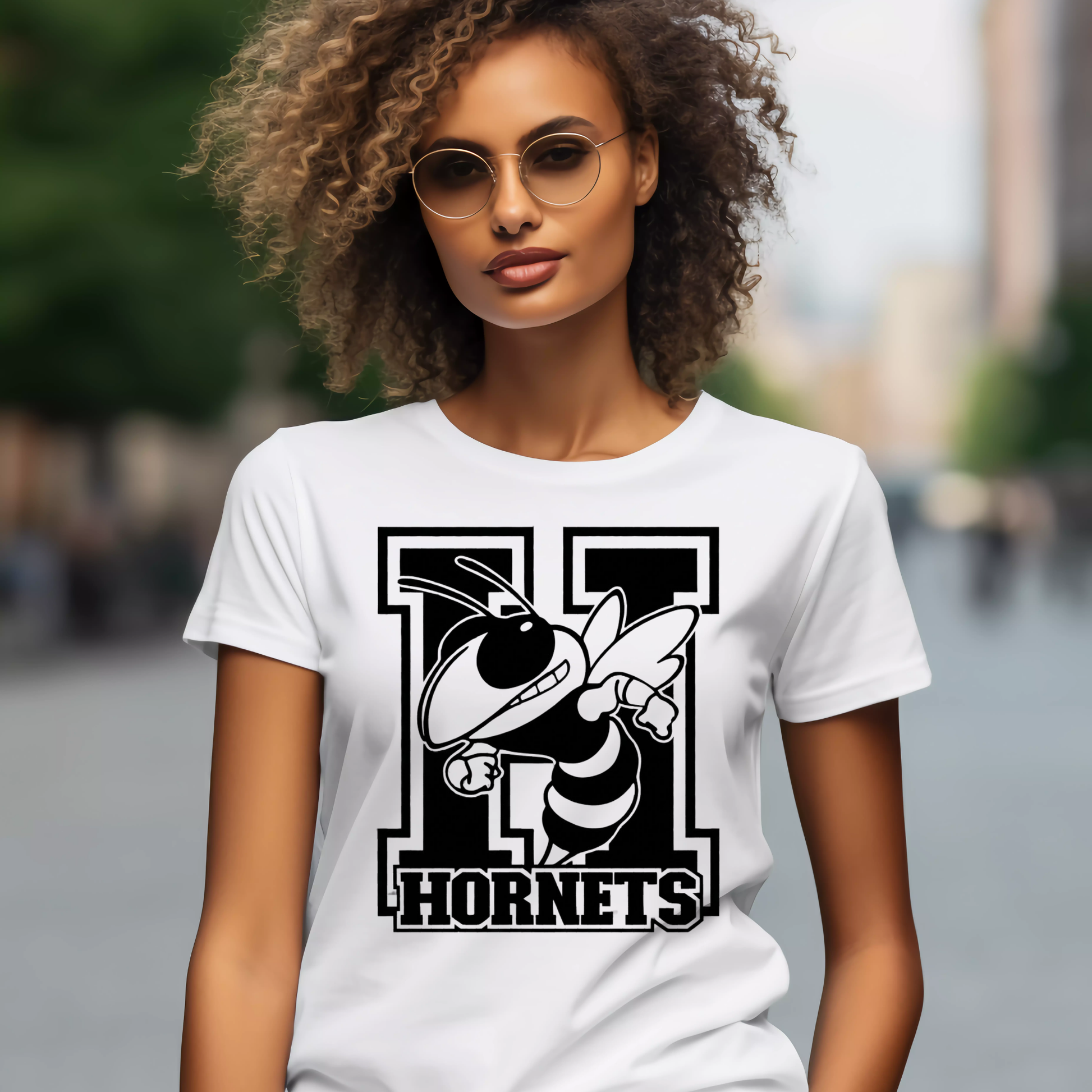 A woman wearing a white short-sleeve T-shirt with a large black and white hornet graphic and the word "HORNETS" on the front, photographed outdoors with a blurred city background.